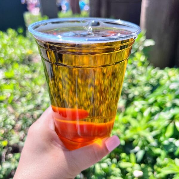 Hand holding a refreshing amber-colored drink in a clear plastic cup outdoors.