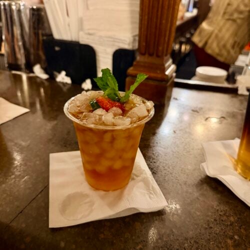 Pimm's Cup in a plastic cup with crushed ice, strawberry, cucumber, and mint on the bar at Rose & Crown Pub in EPCOT