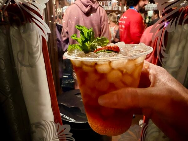 Hand holding a Pimm's Cup at the window of a crowded Rose & Crown Pub at night in EPCOT