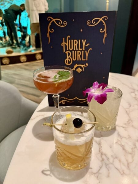 Three Hurly-Burly cocktails on a marble table in front of the menu