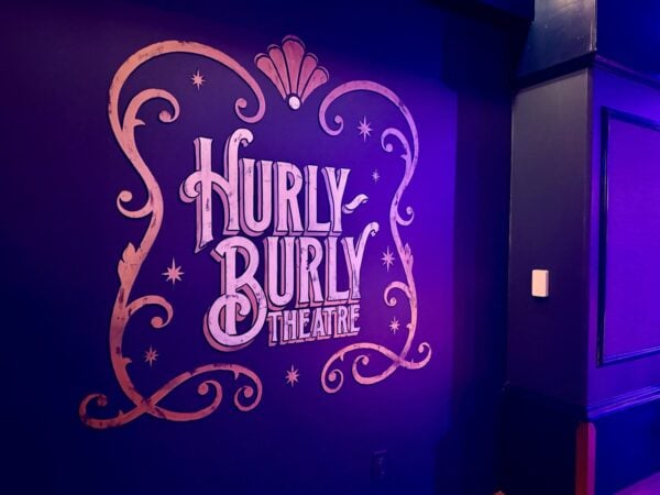 Hurly-Burly Theatre sign painted on a purple-lit wall