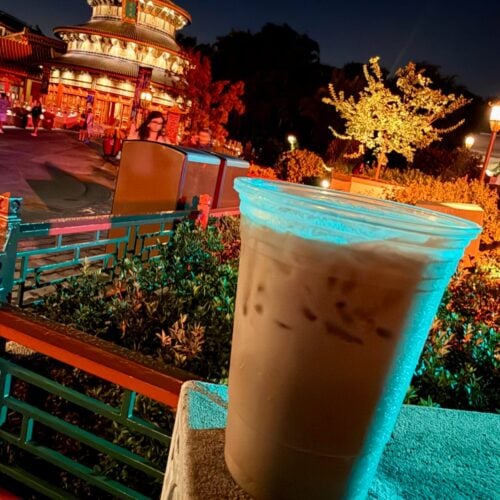 Tipsy Ducks in Love served over ice in a clear cup on a stone ledge, with the lit-up Temple of Heaven at EPCOT's China pavilion behind it