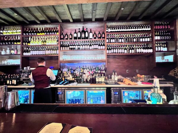 The bar inside Tutto Gusto Wine Cellar at EPCOT, with wine bottles on dark wood shelves